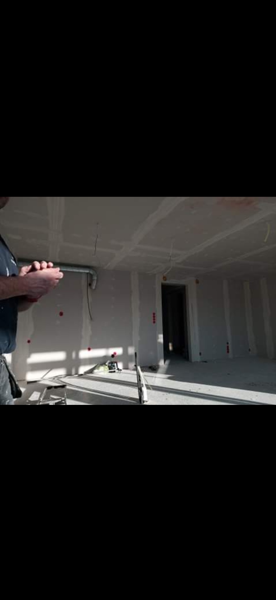 Wnętrze w trakcie prac wykończeniowych: ściany z płyt karton-gips, widoczne narzędzia i instalacje. Jasne światło podkreśla surowość przestrzeni.