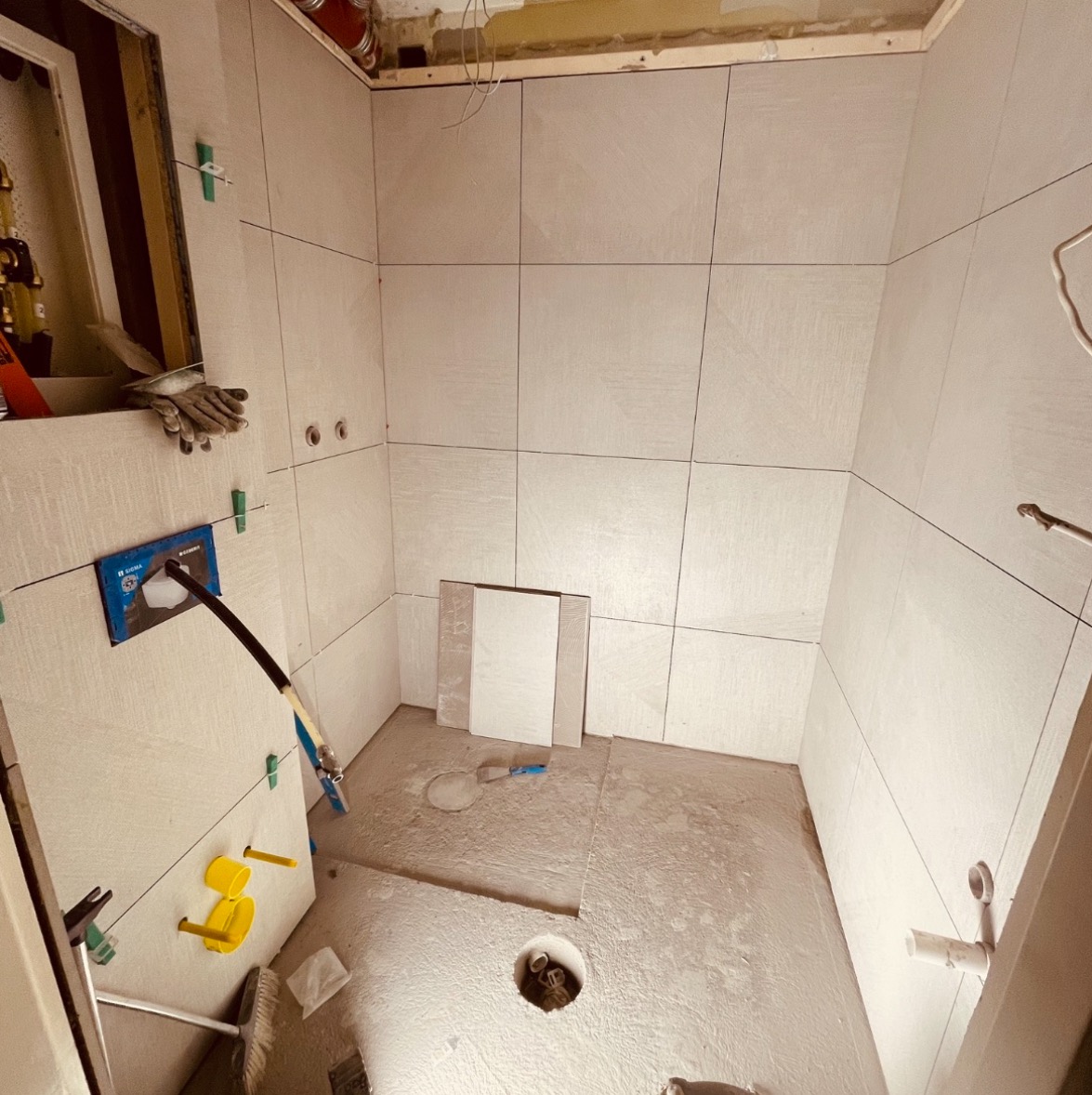 Wnętrze łazienki w trakcie prac glazurniczych: jasne płytki ścienne z systemem poziomowania, przygotowane podłoże pod posadzkę, widoczne narzędzia i akcesoria montażowe.
