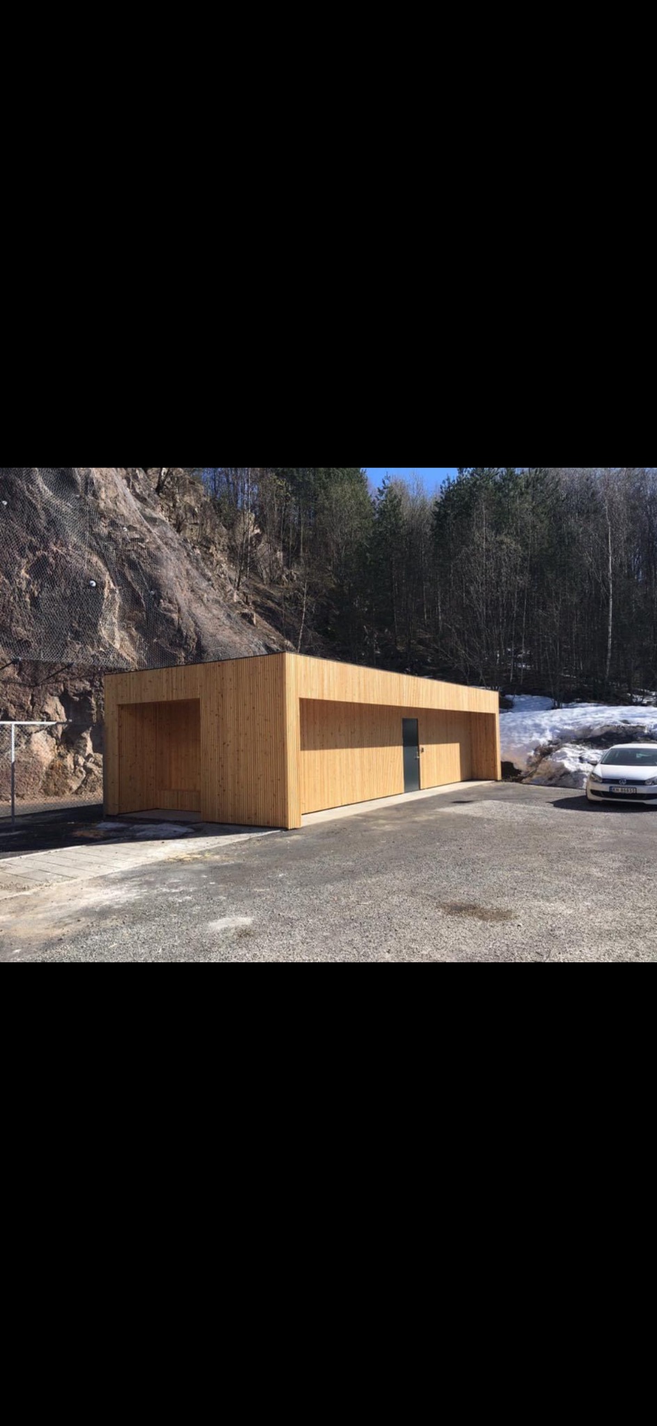 Nowoczesna, drewniana konstrukcja z płaskim dachem na tle skalistej góry i lasu. Minimalistyczny design, naturalne materiały, szara, metalowa brama.