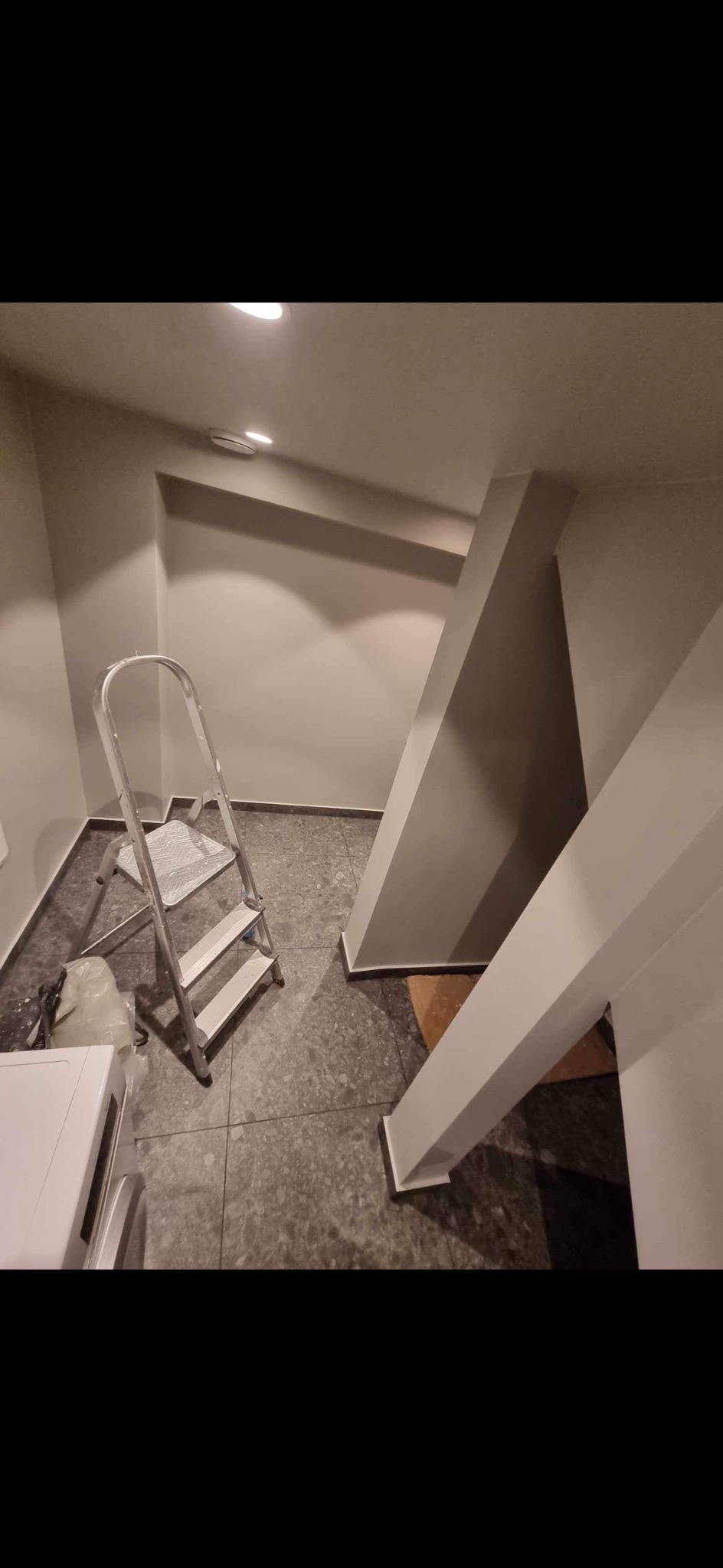 Wnętrze po malowaniu: szara ściana, drabina malarska, widoczne pomalowane elementy konstrukcyjne, szara podłoga. Świeżo odmalowane pomieszczenie.