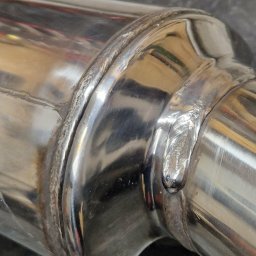WELD IT-Mobilny Spawacz Ostrołęka - Błyszczące, metalowe rury połączone precyzyjnym spawem, widoczne detale spoiny i odbicia światła na gładkiej powierzchni metalu. Makro zbliżenie na łączenie.