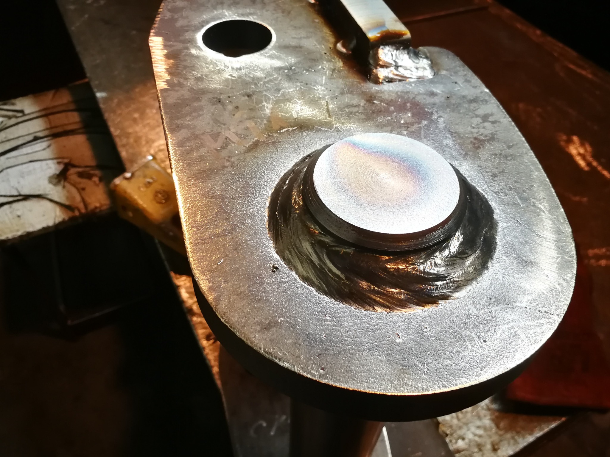 Metalowy element z widocznym spawem wokół okrągłego elementu, ukazujący precyzję wykonania i solidność połączenia. Widoczne ślady obróbki.