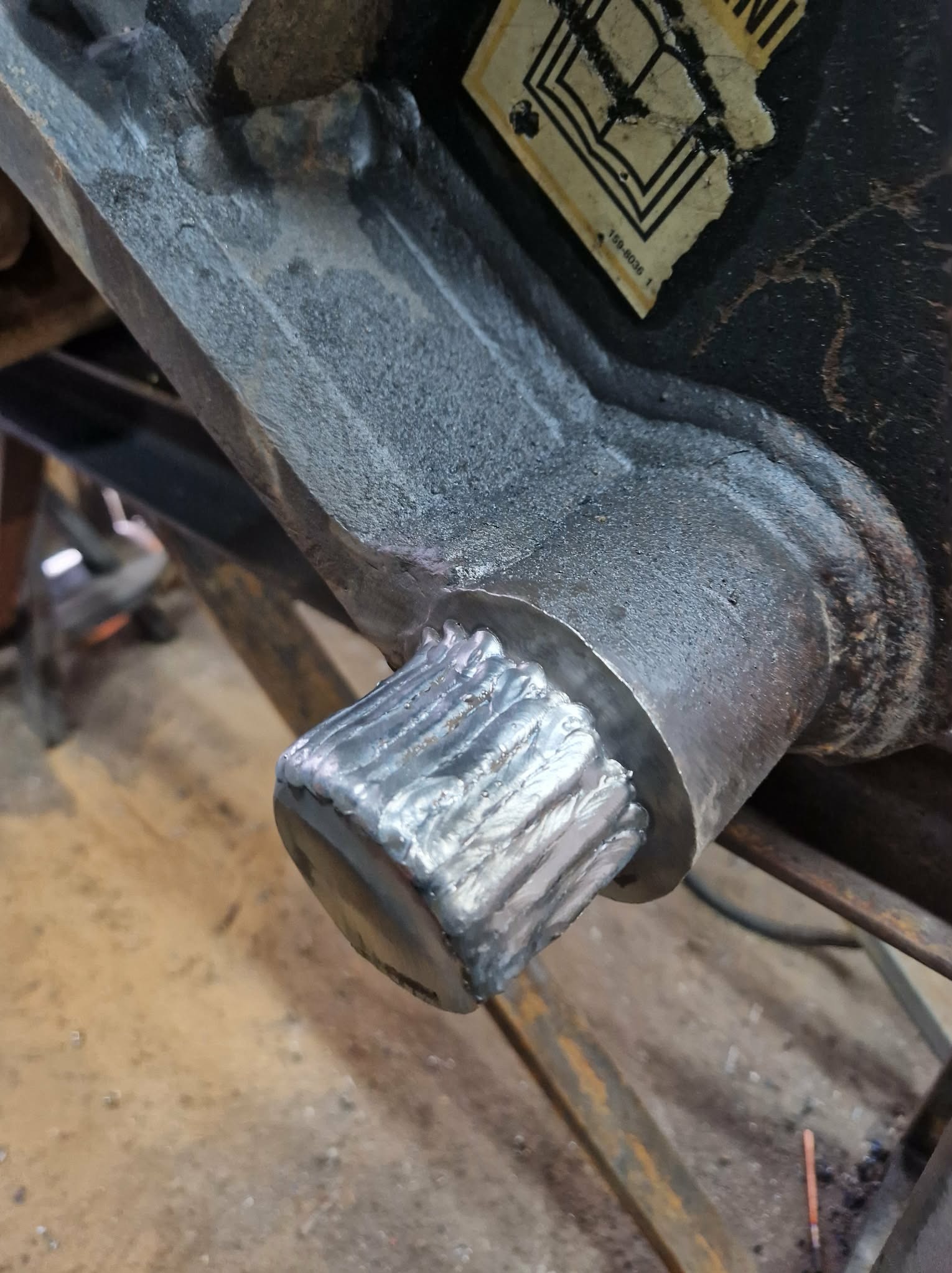 Detal spawu na metalowej konstrukcji. Widoczne ślady po spawaniu i fragment etykiety. Bliskie ujęcie na łączenie elementów.