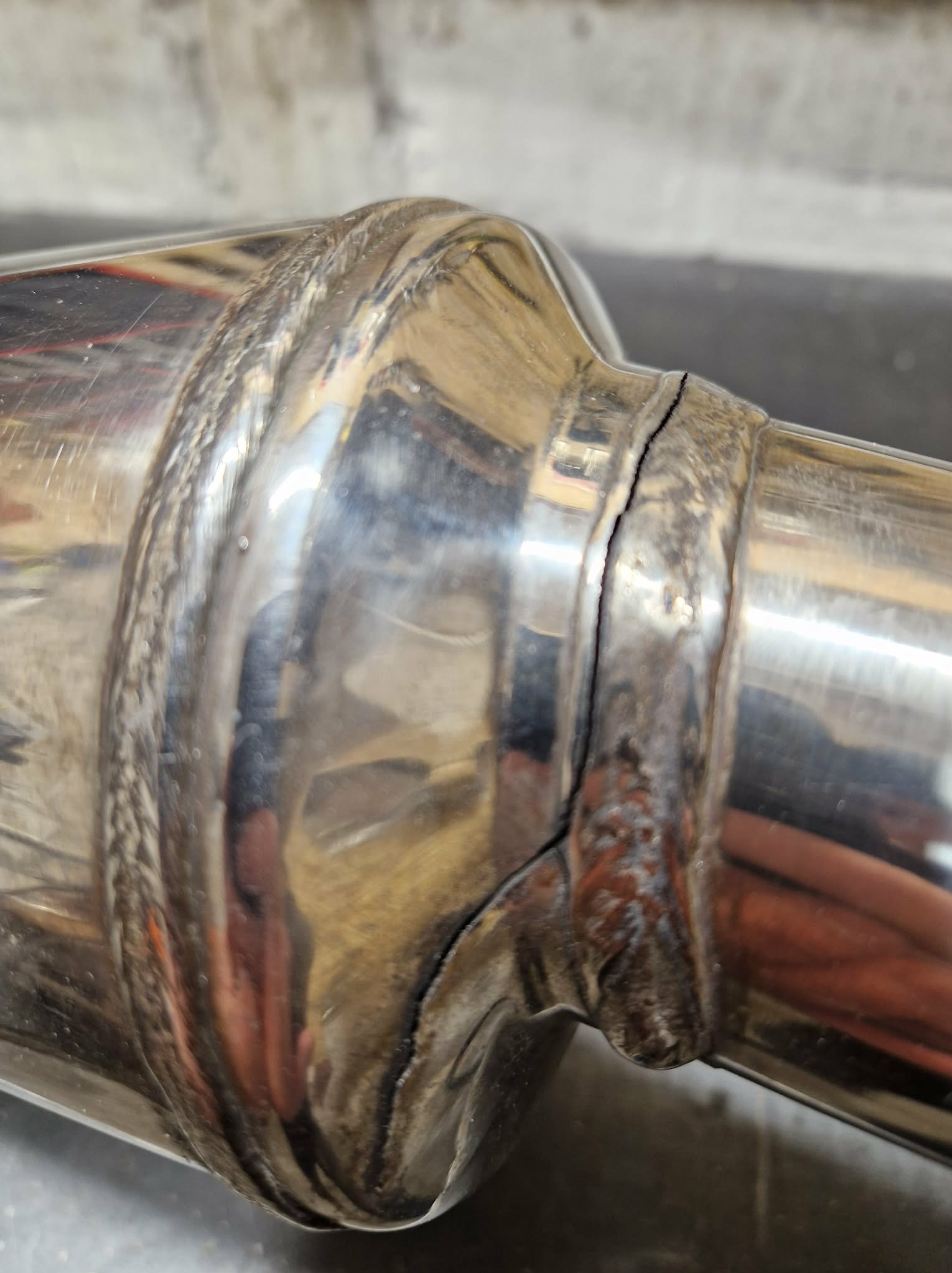 Błyszcząca, spawana rura ze stali nierdzewnej z widocznym pęknięciem w miejscu spawu, ukazująca potencjalną potrzebę naprawy lub wzmocnienia konstrukcji.