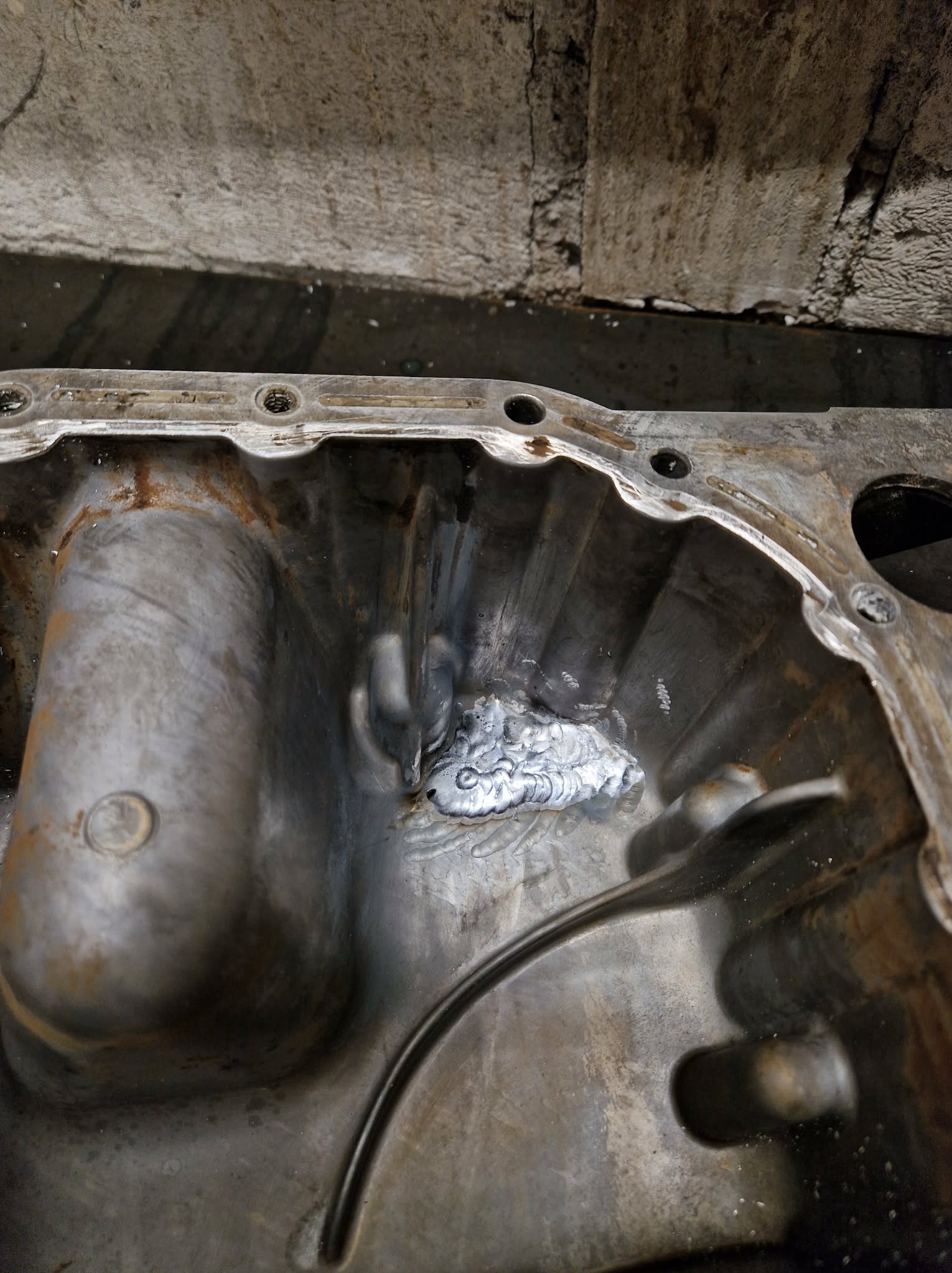 Szczegółowe ujęcie spawu wewnątrz metalowej miski olejowej, ukazujące precyzję i jakość wykonanej naprawy. Widoczne ślady obróbki i surowy wygląd metalu.