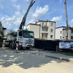 Grupa Almar Serwis Sp. z o.o. - Betonomieszarka HTB z wysięgnikiem pompy betonu na tle budynków mieszkalnych i ogrodzenia z banerem reklamowym dostawcy betonu Almar Serwis.