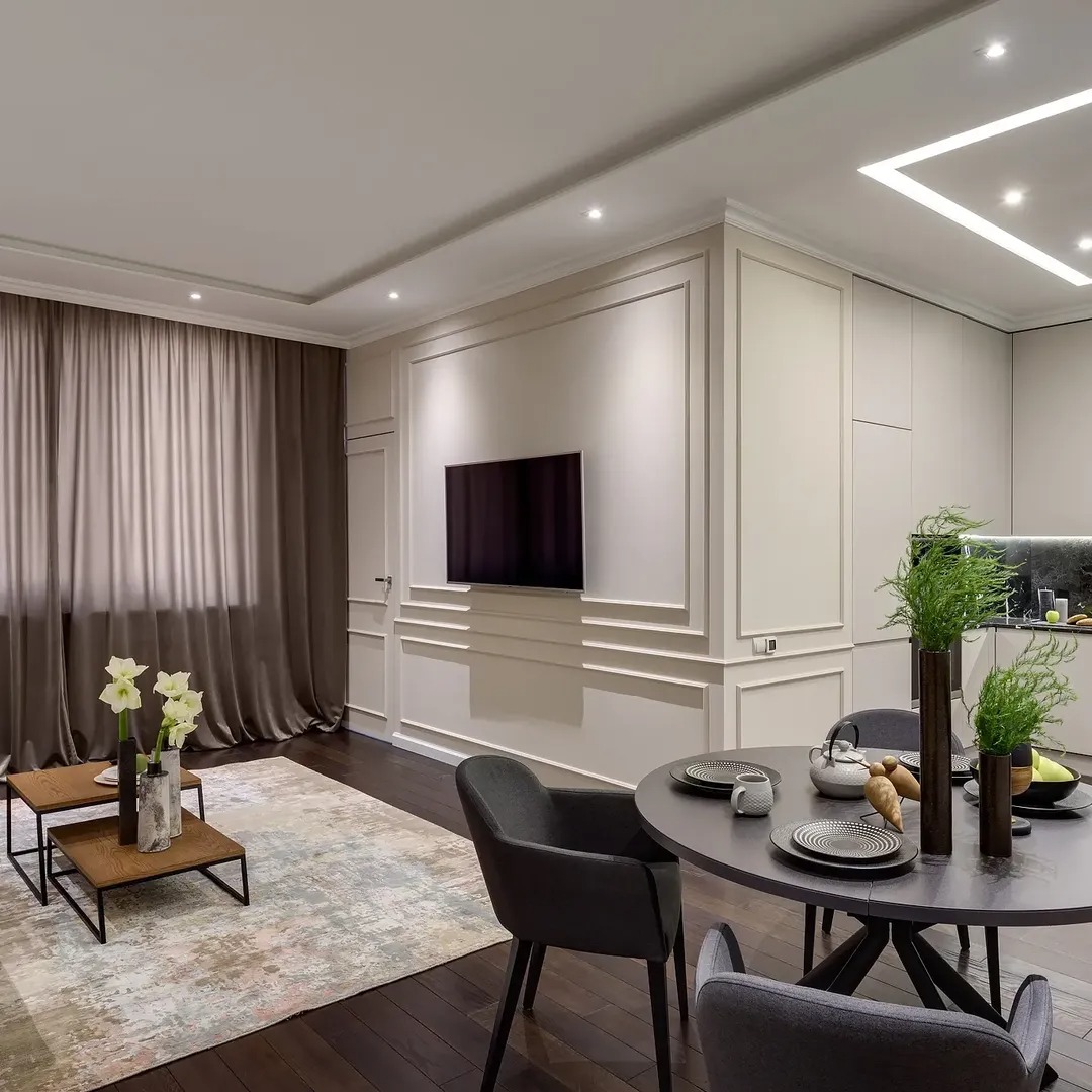 Eleganckie wykończenie wnętrza salonu z jadalnią: ciemna podłoga, sztukateria na ścianach, minimalistyczne meble i dekoracje. Nowoczesne oświetlenie sufitowe.