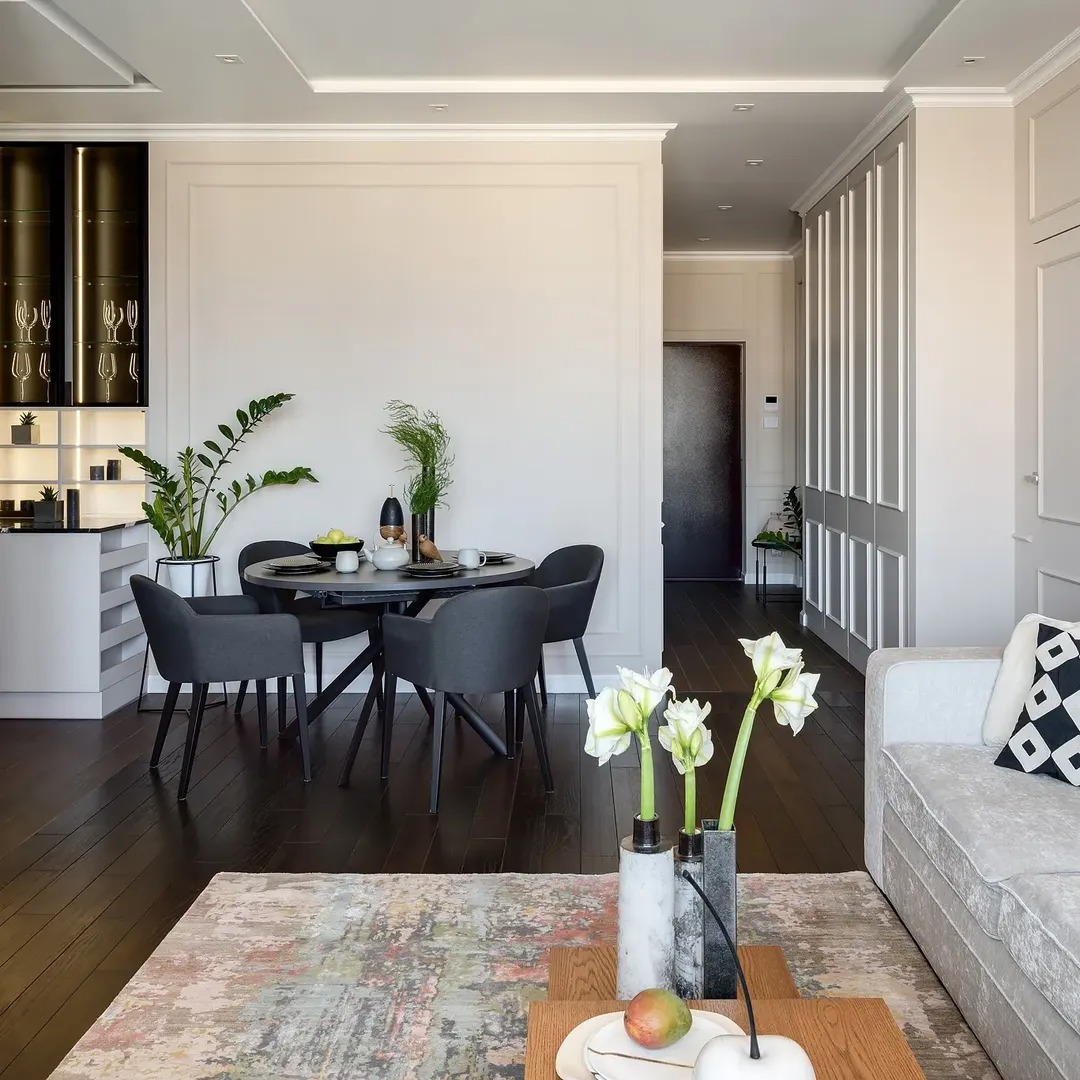 Eleganckie wnętrze: ciemna podłoga, okrągły stół z krzesłami, dekoracje roślinne, sofa z wzorzystą poduszką i dywan w stonowanych barwach. Minimalistyczny design.