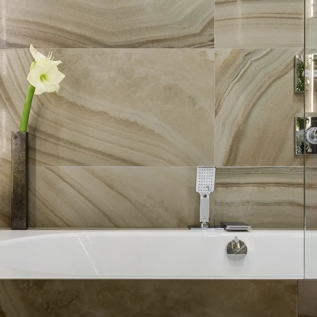 Elegancka łazienka w Warszawie: beżowe płytki imitujące marmur, biała wanna, chromowana armatura i amarylis w wazonie. Minimalistyczny design.