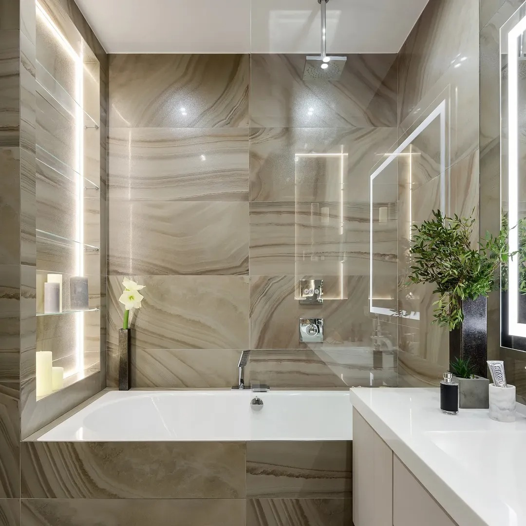 Elegancka łazienka z wanną, płytkami imitującymi marmur i oświetleniem LED. Minimalistyczny design z akcentami roślinnymi i szklanymi półkami.