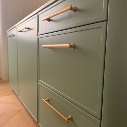 Konrad Nizioł - Zielona zabudowa kuchenna z drewnianymi uchwytami na tle parkietu w jodełkę. Ujęcie z dołu podkreśla nowoczesny design i dbałość o detale.