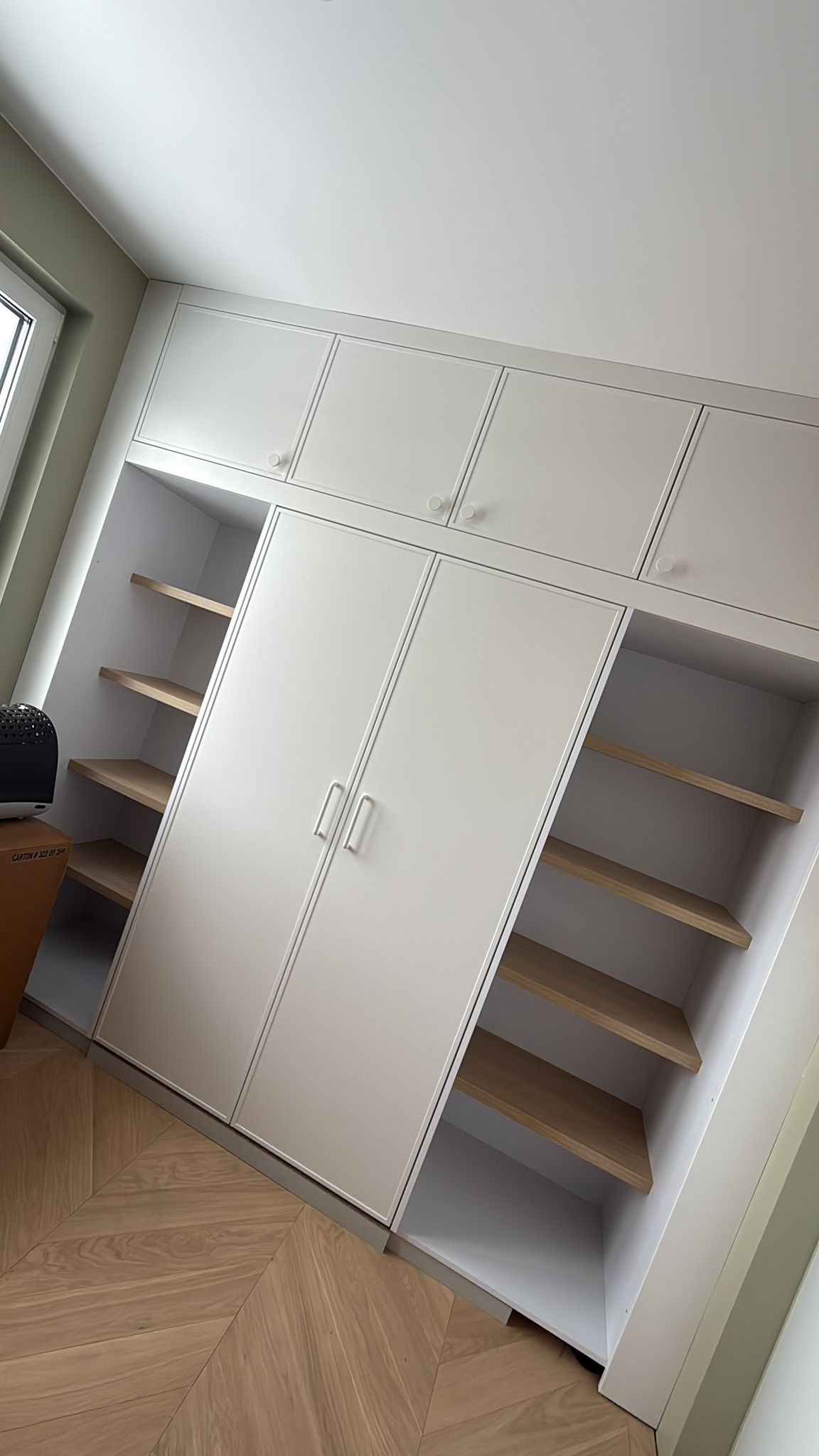 Biała szafa wnękowa z drewnianymi półkami, widok z dołu, parkiet w jodełkę na podłodze. Minimalistyczny design, jasne wnętrze, nowoczesne wykończenie.