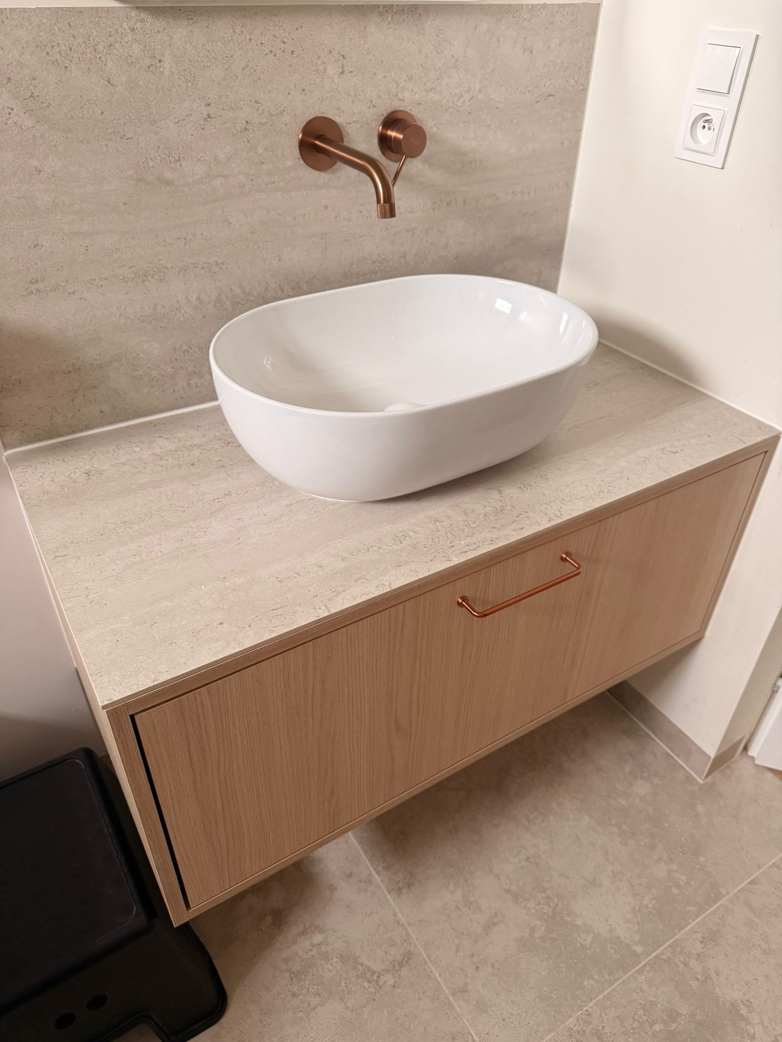 Nowoczesna łazienka: biała umywalka nablatowa na szafce z jasnego drewna, miedziana bateria ścienna i beżowe płytki. Minimalistyczny design.