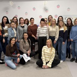 Przedszkole Teddy - Grupowe zdjęcie uśmiechniętych kobiet, prawdopodobnie pracowniczek żłobka, stojących i klęczących na tle ściany z dekoracjami w kształcie truskawek i śnieżynek.