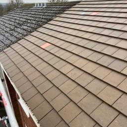 GlancMycie - Częściowo wyczyszczony dach z brązowej dachówki, widoczne rusztowanie i fragment elewacji z cegły. Po lewej stronie dach pokryty mchem, po prawej czysty.