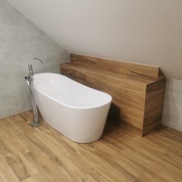 Usługi glazurnicze - Nowoczesna łazienka na poddaszu z wolnostojącą wanną, drewnopodobną zabudową i płytkami imitującymi drewno na podłodze. Minimalistyczny design.