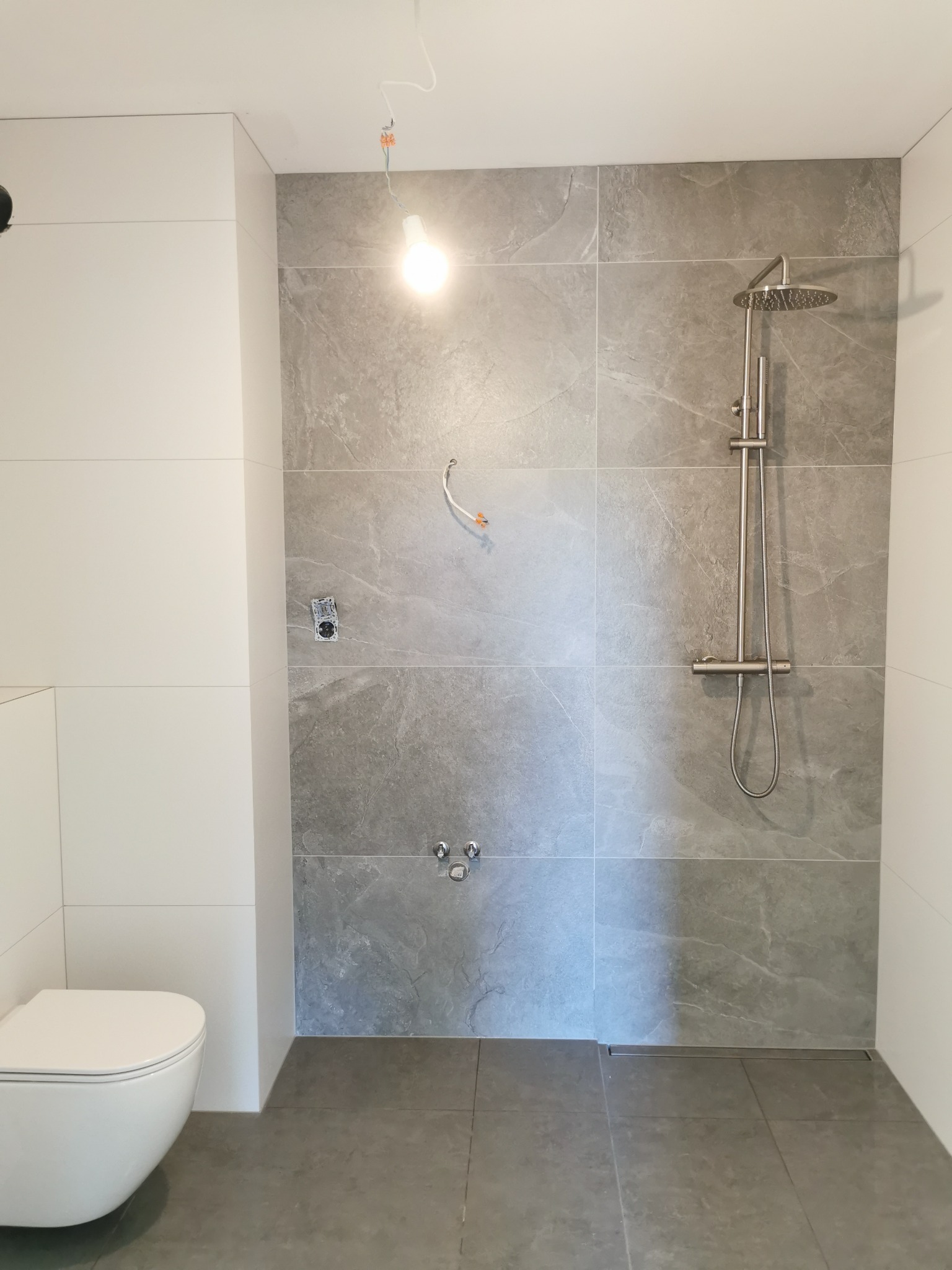 Nowoczesna łazienka w Krotoszynie z szarymi płytkami imitującymi kamień, białą armaturą i deszczownicą. Minimalistyczny design, surowy styl.