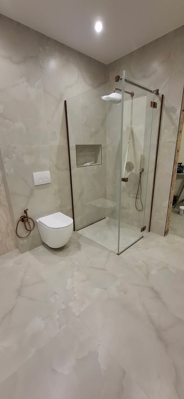 Elegancka łazienka z kabiną prysznicową typu walk-in, wykończona płytkami imitującymi marmur. Uwagę zwracają detale w kolorze miedzianym: rama kabiny, uchwyt na ręcznik.