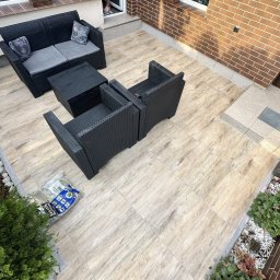 ADMIN ANNA LAUDAŃSKA - Wykończony taras z nowymi płytkami imitującymi drewno, czarne meble ogrodowe, częściowo zachowane stare płytki na schodach, widoczna hydroizolacja.