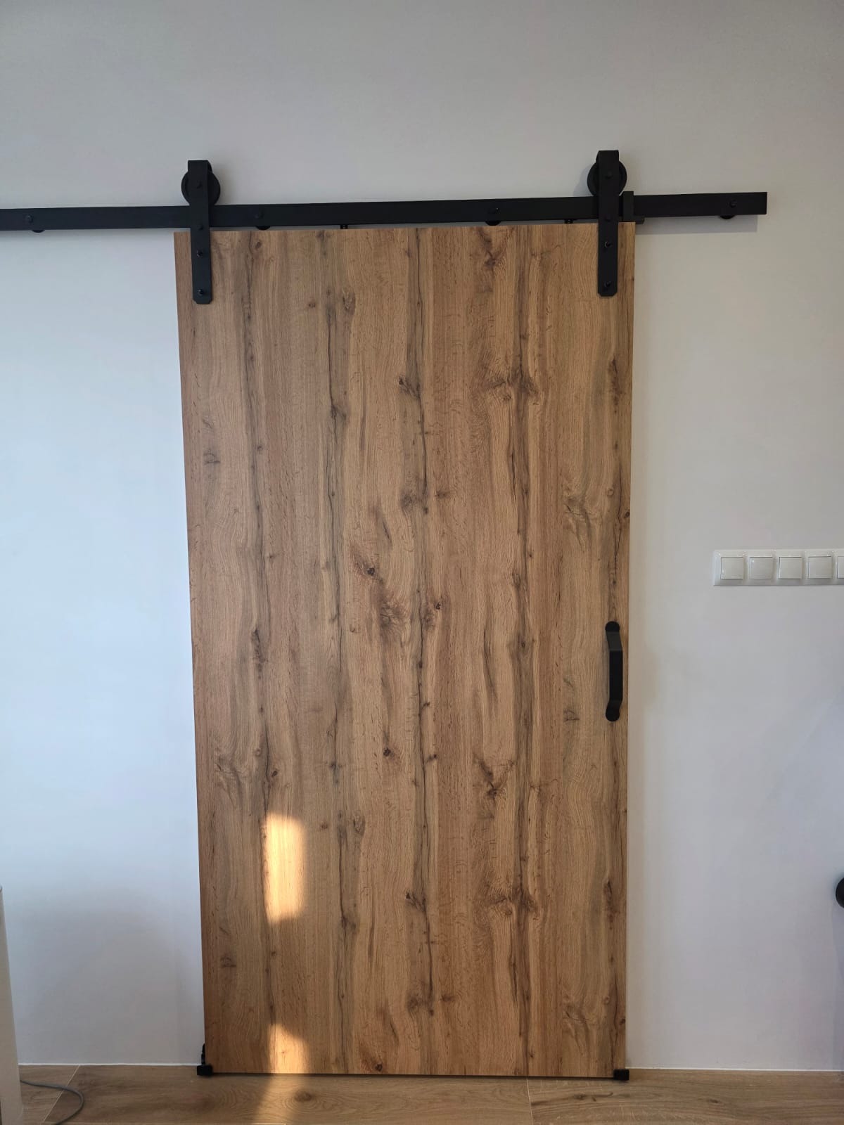 Drewniane drzwi przesuwne w stylu rustykalnym z czarnym, metalowym systemem zawieszenia. Widoczne detale faktury drewna i minimalistyczny uchwyt.