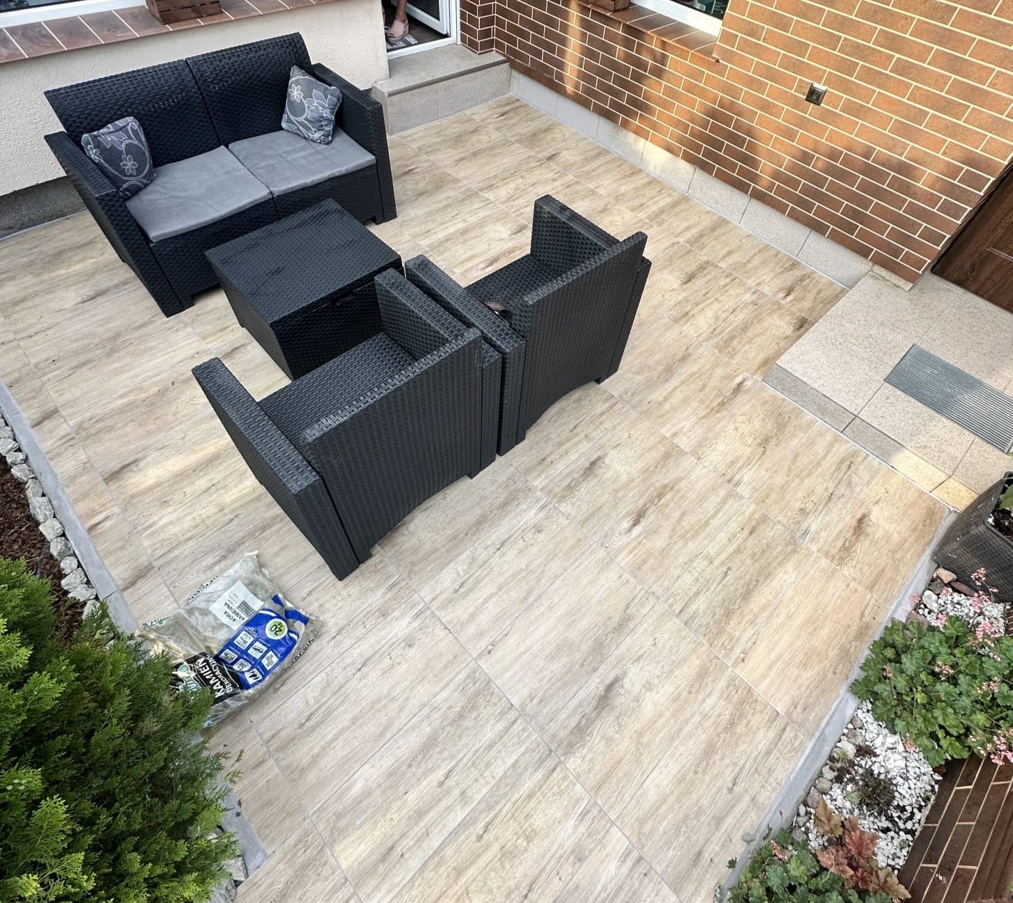 Wykończony taras z nowymi płytkami imitującymi drewno, czarne meble ogrodowe, częściowo zachowane stare płytki na schodach, widoczna hydroizolacja.