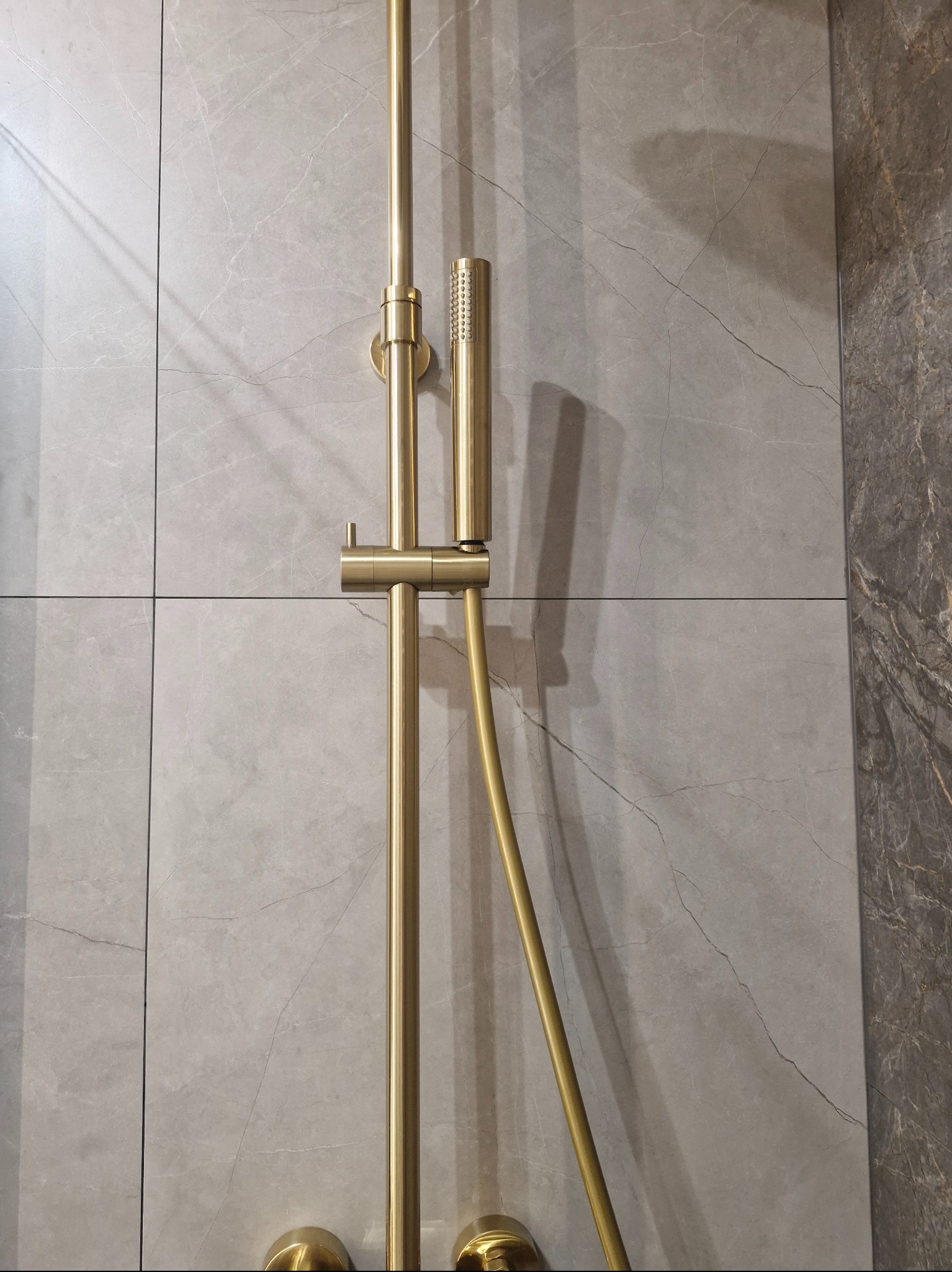 Złota armatura natryskowa na tle szarych, marmurkowych płytek. Nowoczesny design łazienki po remoncie, z dbałością o detale i estetykę wykończenia.