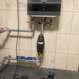 ARIONEX SPÓŁKA Z OGRANICZONĄ ODPOWIEDZIALNOŚCIĄ - Instalacja kotła Buderus z zaworami Trinity i filtrem Flamco, rury wypoziomowane poziomicą Lux-Tools. Widoczne narzędzia hydrauliczne na podłodze.