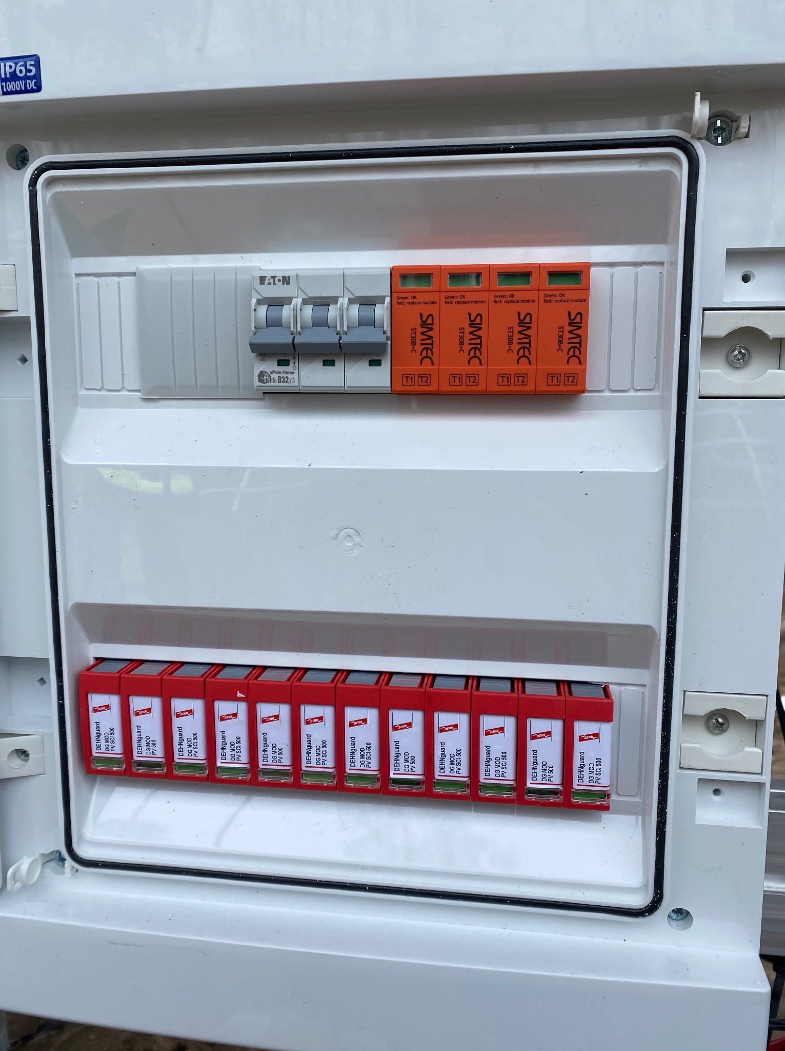 Rozdzielnica DC z zabezpieczeniami przepięciowymi DEHNguard i SIMTEC, instalacja fotowoltaiczna. Widoczne moduły i wyłącznik Eaton. Szczegółowe ujęcie.