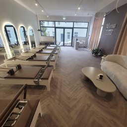Konrad Pfeiffer - Jasne studio pilates z parkietem w jodełkę, rzędem maszyn do ćwiczeń i minimalistycznym wystrojem. Duże okna wpuszczają naturalne światło.