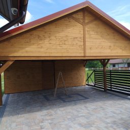 BaliHouse - Drewniana konstrukcja z zadaszeniem i przyległym ogrodzeniem panelowym na kostce brukowej. Widoczna drabina oparta o ścianę. Ujęcie w słoneczny dzień.