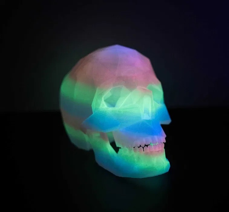 Wielobarwna, półprzezroczysta czaszka, wydrukowana w technologii 3D, o geometrycznej fakturze, oświetlona od wewnątrz, na czarnym tle.