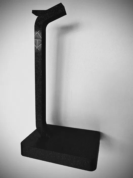 Czarny, matowy stojak na słuchawki z widocznym wzorem geometrycznym, wydrukowany w technologii addytywnej. Minimalistyczny design na tle jasnej ściany.