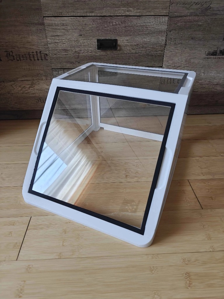 Biała, trójwymiarowa, przezroczysta obudowa z czarną ramką, prawdopodobnie wykonana metodą addytywną, na drewnianym podłożu. Widoczne warstwy druku.