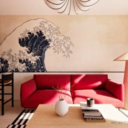 PROJEKTOWANIE WNĘTRZ Adrianna Lis - Salon z czerwoną sofą i ścianą z motywem fali, inspirowany stylem japońskim. Na stoliku wazon i książki. Widoczna lampa z abażurem z rattanu i krzesła barowe.