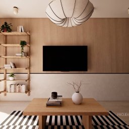 PROJEKTOWANIE WNĘTRZ Adrianna Lis - Jasne wnętrze salonu z drewnianą ścianą, półkami na książki i rośliny. Na pierwszym planie stolik kawowy z dekoracjami i czarno-biały dywan w paski.