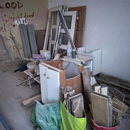 Przeprowadzki - Opróżnione pomieszczenie z meblami, drzwiami i odpadami budowlanymi. Na ścianie widoczne napisy. W tle drabina. Ujęcie z bliska, w słabym oświetleniu.