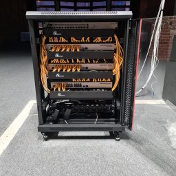 SKSYSTEMS SPÓŁKA Z OGRANICZONĄ ODPOWIEDZIALNOŚCIĄ - Otwarta szafa rack z zamontowanymi routerami, switchami i okablowaniem. Widoczne urządzenia marki GetFort i MikroTik. Kable patchcord w kolorze żółtym.