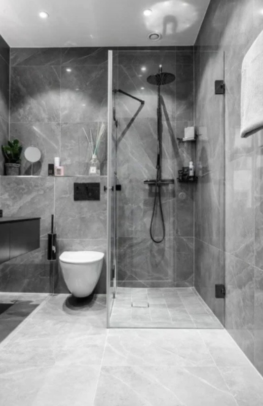 Nowoczesna łazienka w szarościach z kabiną typu walk-in, deszczownicą i marmurowymi płytkami. Minimalistyczny design z akcentami czerni i subtelnym oświetleniem.