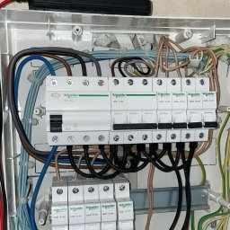 BK-Elektro Bartosz Klamecki - Rozdzielnia elektryczna Schneider Electric z bezpiecznikami i przewodami w różnych kolorach, zamontowana w białej obudowie. Widoczne ślady montażu na ścianie.