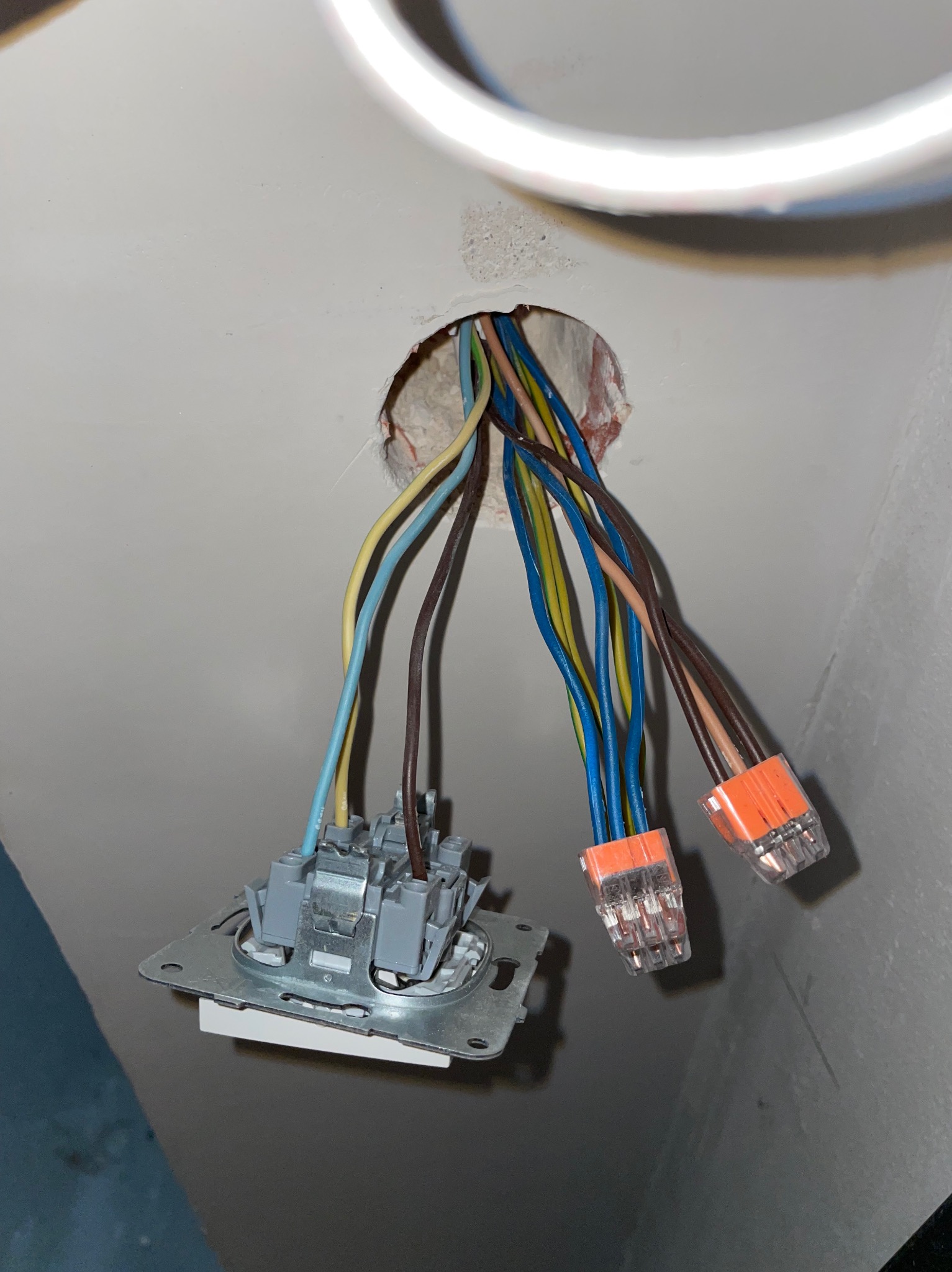 Niezabezpieczone przewody elektryczne wystające ze ściany, podłączone do złączek WAGO i gniazdka, widoczne ślady po wierceniu w ścianie.