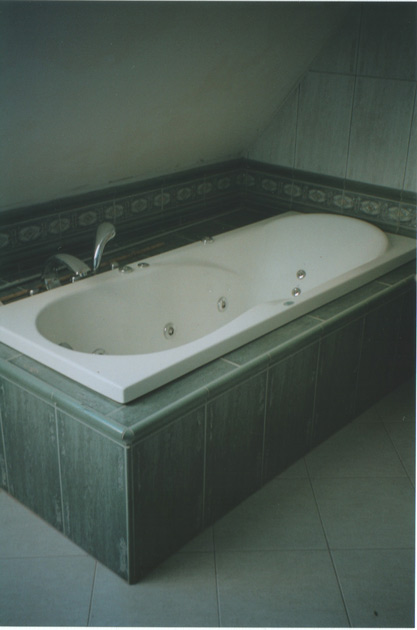 Wanna z hydromasażem obudowana ciemnozielonymi płytkami w łazience na poddaszu, widoczny chromowany kran i dysze do hydromasażu.