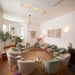 Prywatny Ośrodek Terapii Uzależnień Space Therapy Wielkopolska - Jasne wnętrze z krzesłami ustawionymi w kręgu na jutowym dywanie, małe stoliki, kominek i rośliny doniczkowe tworzą przytulną atmosferę spotkań grupowych.