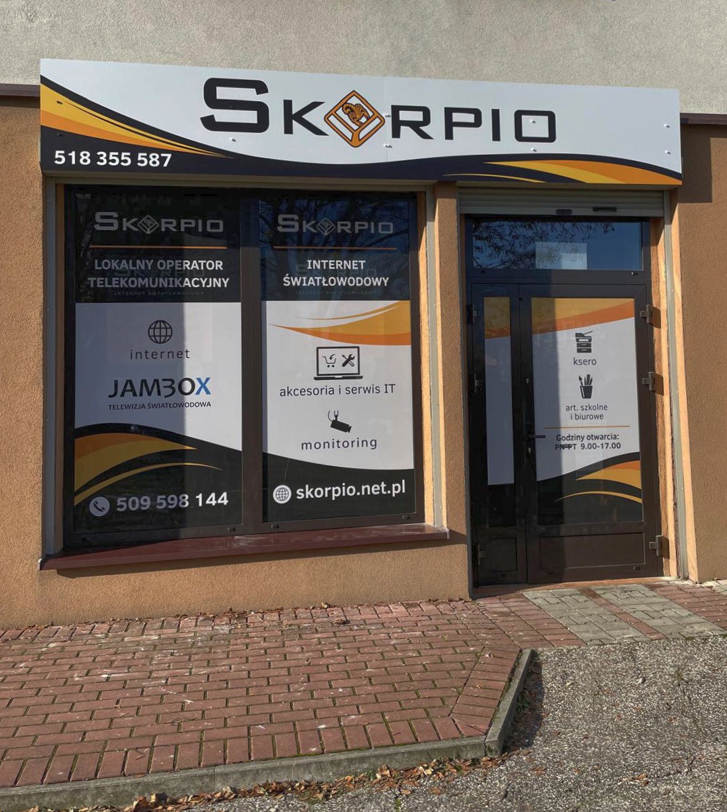 Fasada budynku firmy telekomunikacyjnej Skorpio z szyldem i oklejonymi szybami, prezentującymi ofertę: internet światłowodowy, telewizja, akcesoria IT i monitoring.
