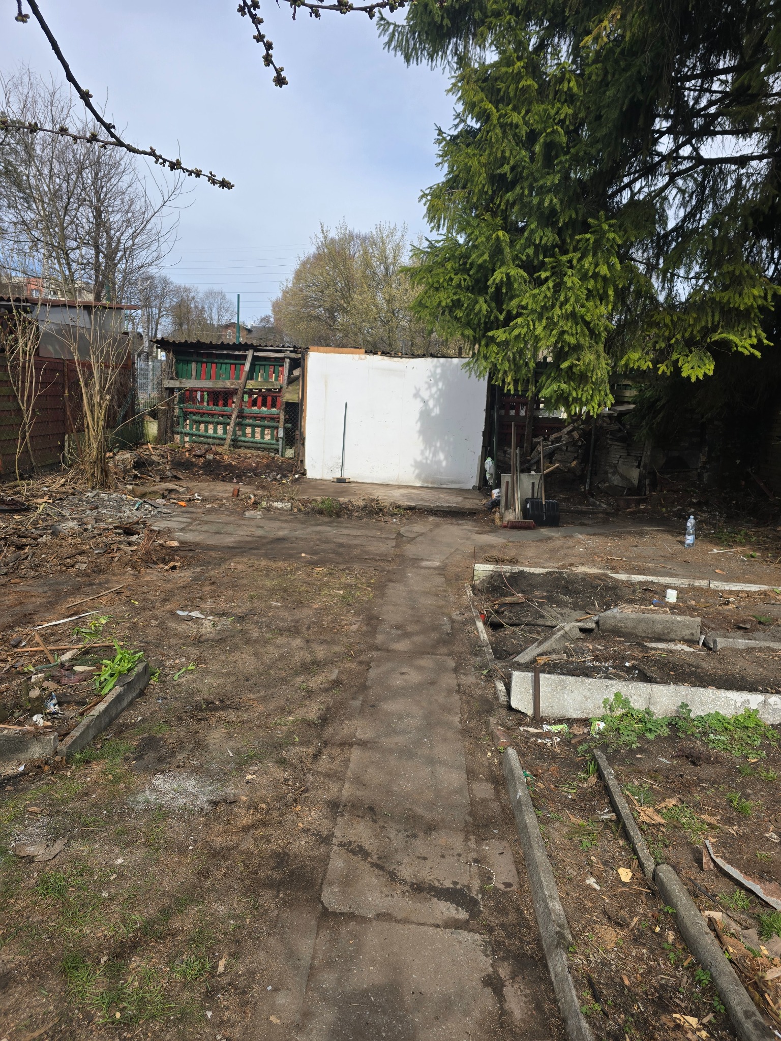 Teren po rozbiórce w Chorzowie: gruz, resztki konstrukcji i ścieżka. Widoczne fragmenty budynków i drzewa. Prace porządkowe po demontażu.