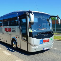OSK POL-CAR Jan Ziemiański - Autobus szkoleniowy Polcar z oznaczeniem 'L' na przodzie, jadący po drodze w słoneczny dzień. Widoczni instruktor i kursant za kierownicą.