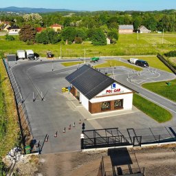 OSK POL-CAR Jan Ziemiański - Widok z lotu ptaka na plac manewrowy szkoły jazdy z budynkiem biura, pojazdami i elementami infrastruktury szkoleniowej w otoczeniu zieleni i zabudowań.