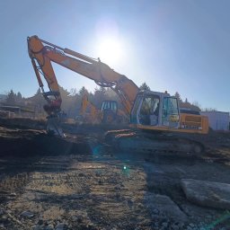 OSK POL-CAR Jan Ziemiański - Żółta koparka Liebherr na placu budowy w słoneczny dzień, z widoczną drugą koparką w tle. Prace ziemne w toku, teren przygotowany pod budowę.