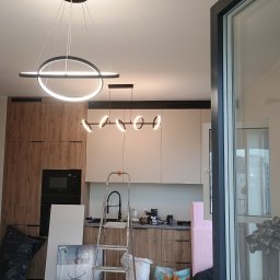 Serhii Novytskyi - Nowoczesne oświetlenie LED w kuchni w trakcie montażu. Widoczna drabina, elementy zabudowy kuchennej i okno. Ujęcie z dołu, podkreślające design lamp.