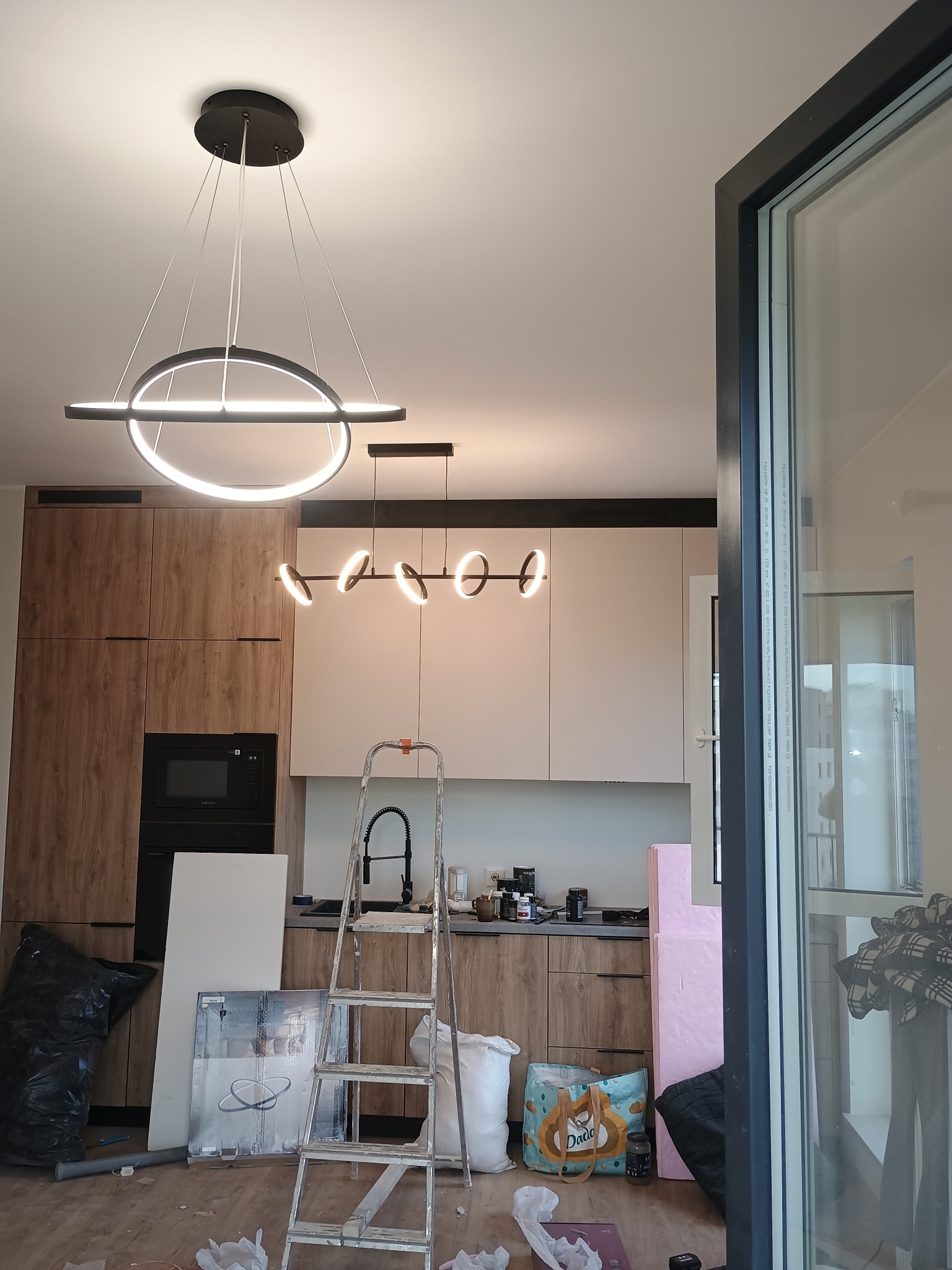 Nowoczesne oświetlenie LED w kuchni w trakcie montażu. Widoczna drabina, elementy zabudowy kuchennej i okno. Ujęcie z dołu, podkreślające design lamp.