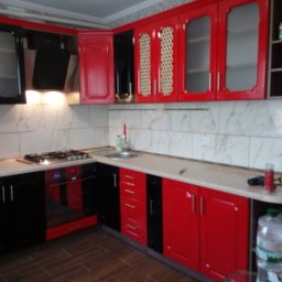 VLADEKBUD - Czerwono-czarna zabudowa kuchenna z błyszczącymi frontami i marmurkową glazurą. Widoczny fragment blatu z akcesoriami. Ujęcie z poziomu podłogi.